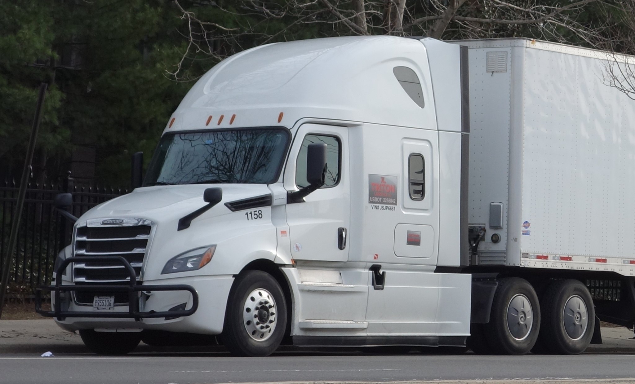 A white Freightliner tractor with an enclosed box trailer parked on a Queens street.