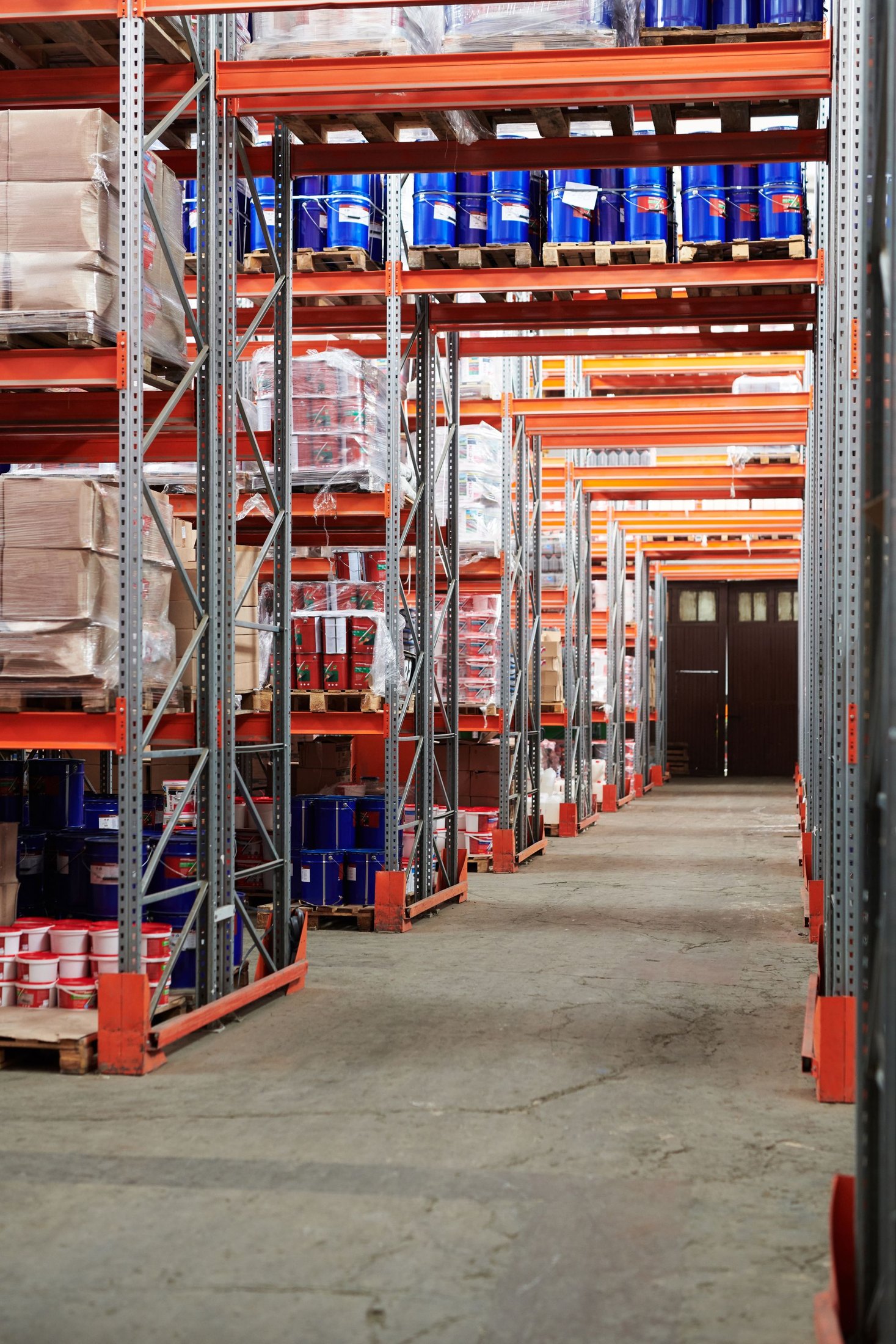 Warehouse pallet racks stocked with cartons and packaged goods beside a concrete aisle.