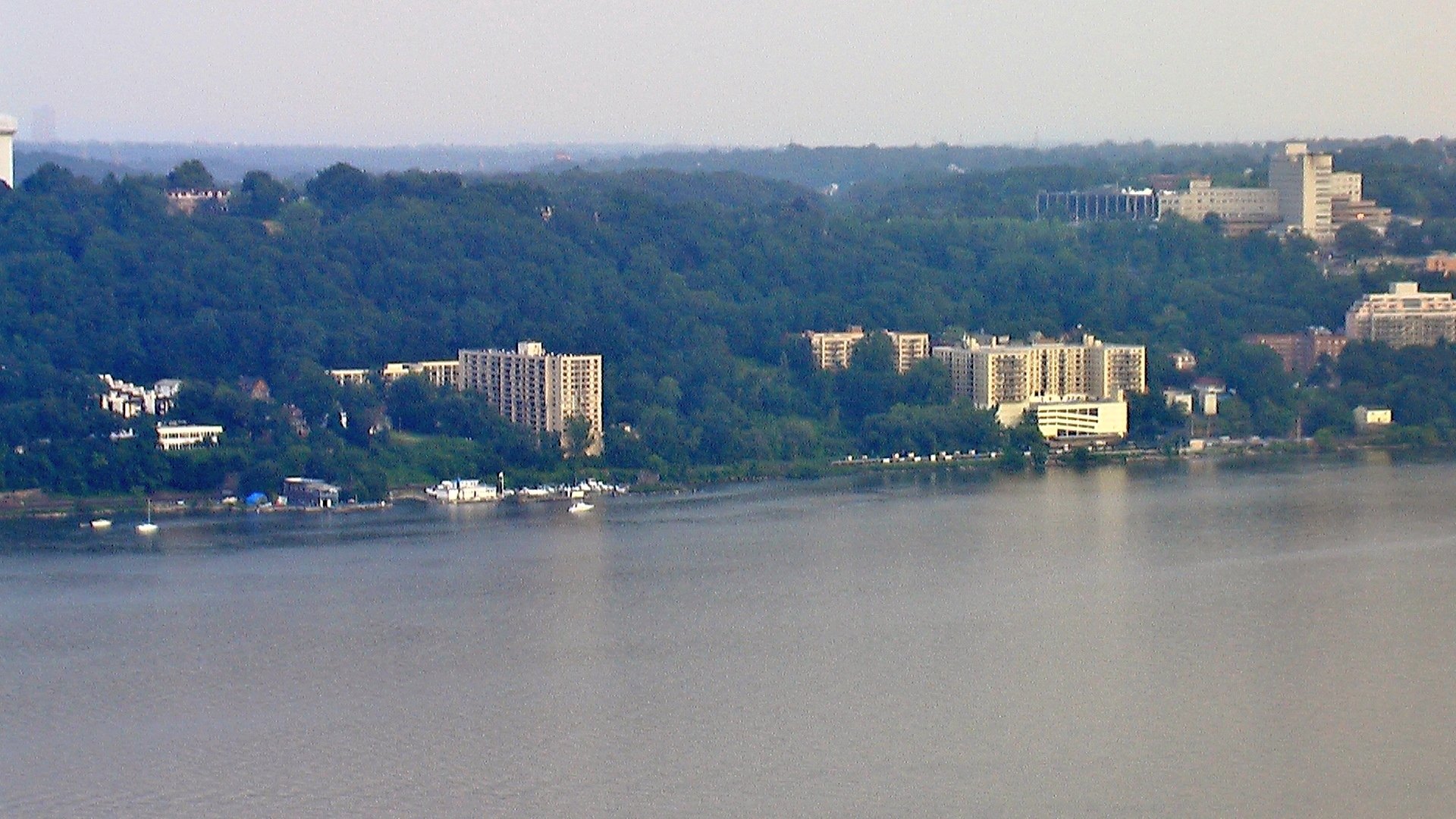 Yonkers buildings and wooded hills along the east bank of the Hudson River, viewed across the water.